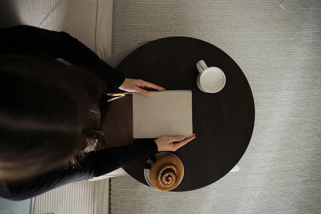 Seen from above, a person taking notes at a round table next to a cup.