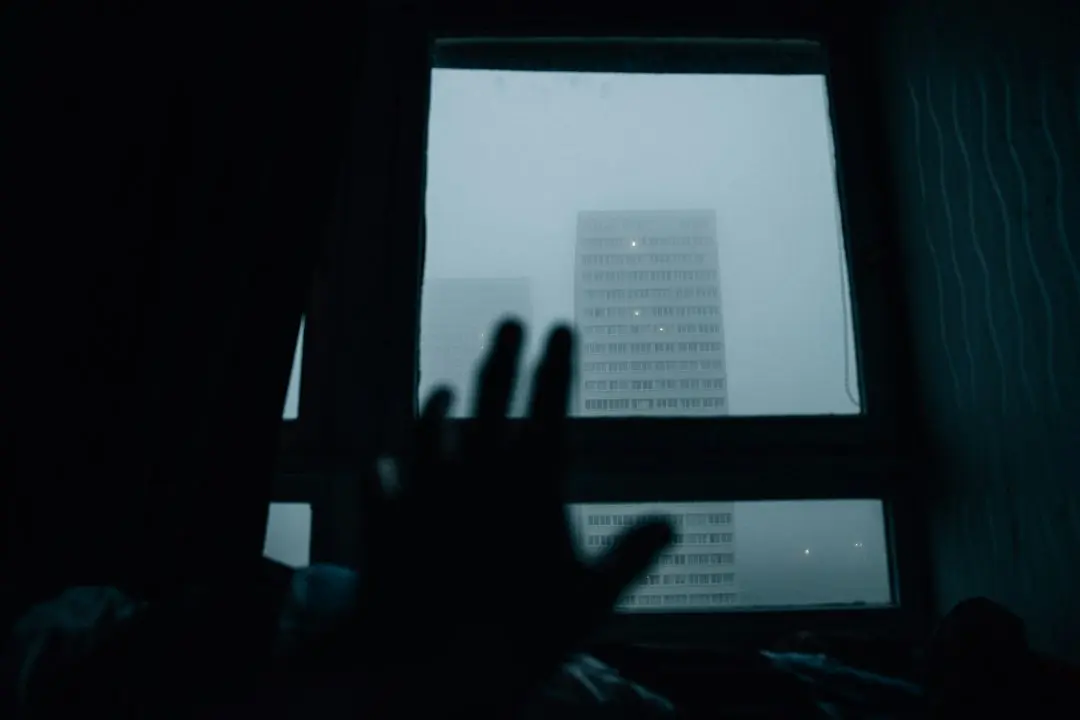 The silhouette of a hand in front of a window in a dark room.